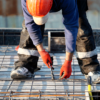 Um trabalhador da construção civil com equipamento de segurança amarra vergalhões em um canteiro de obras