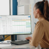 Uma mulher em um escritório analisa dados de acompanhamento de projetos em uma tela de computador exibindo um gráfico de Gantt